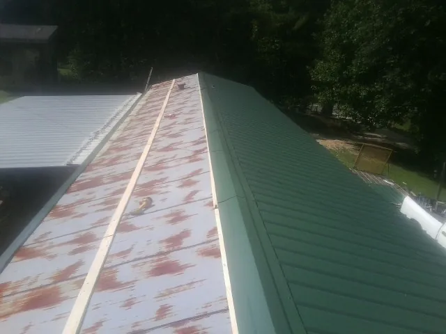 Old rusted panels beside newly installed green metal roofing — Wind Damage Roof Repair by Roofing Brothers in Buena Vista
